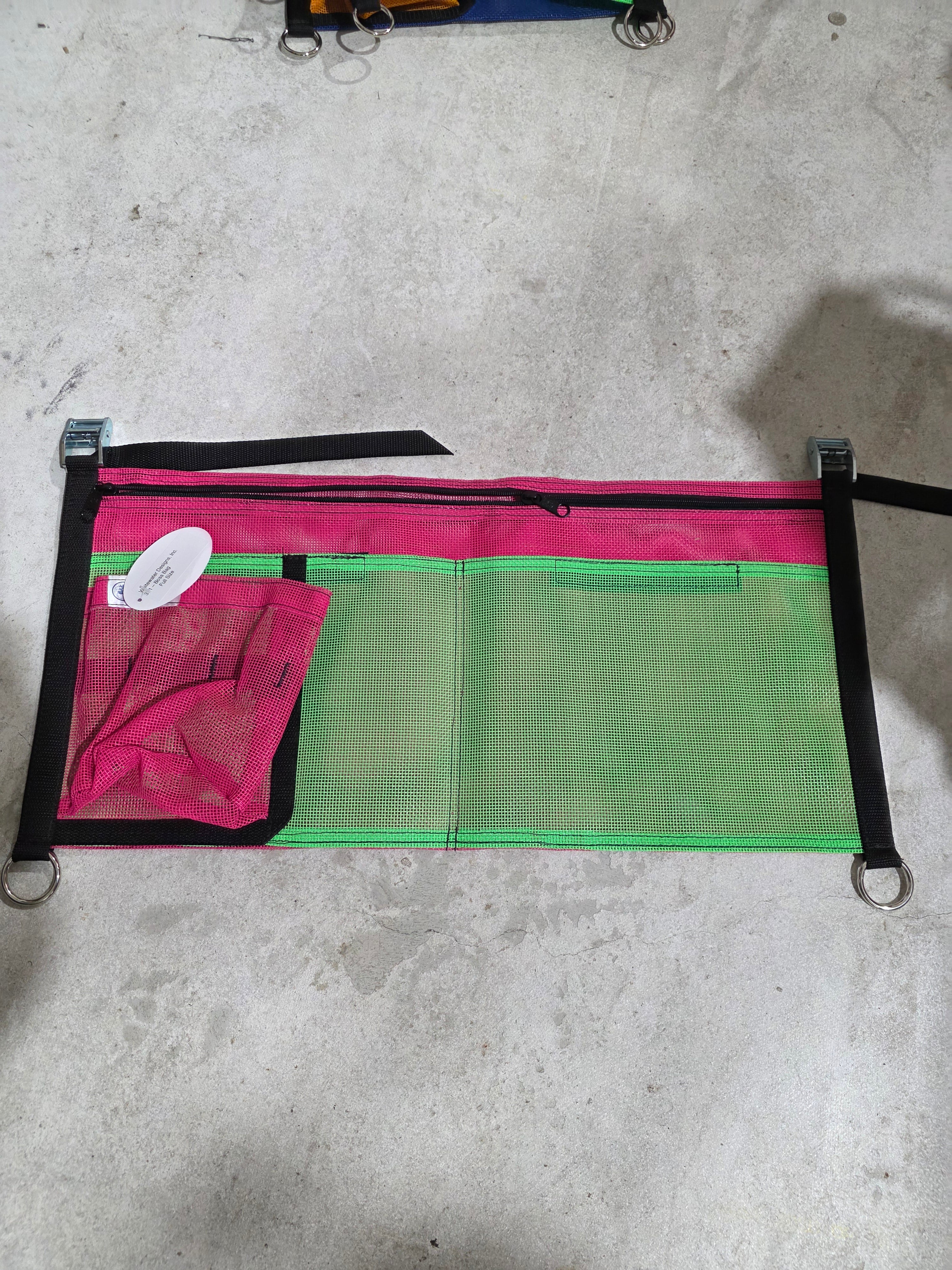 Green and pink mesh bag with black straps on a concrete surface, rafting gear storage