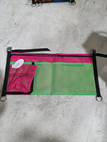 Green and pink mesh bag with black straps on a concrete surface, rafting gear storage 